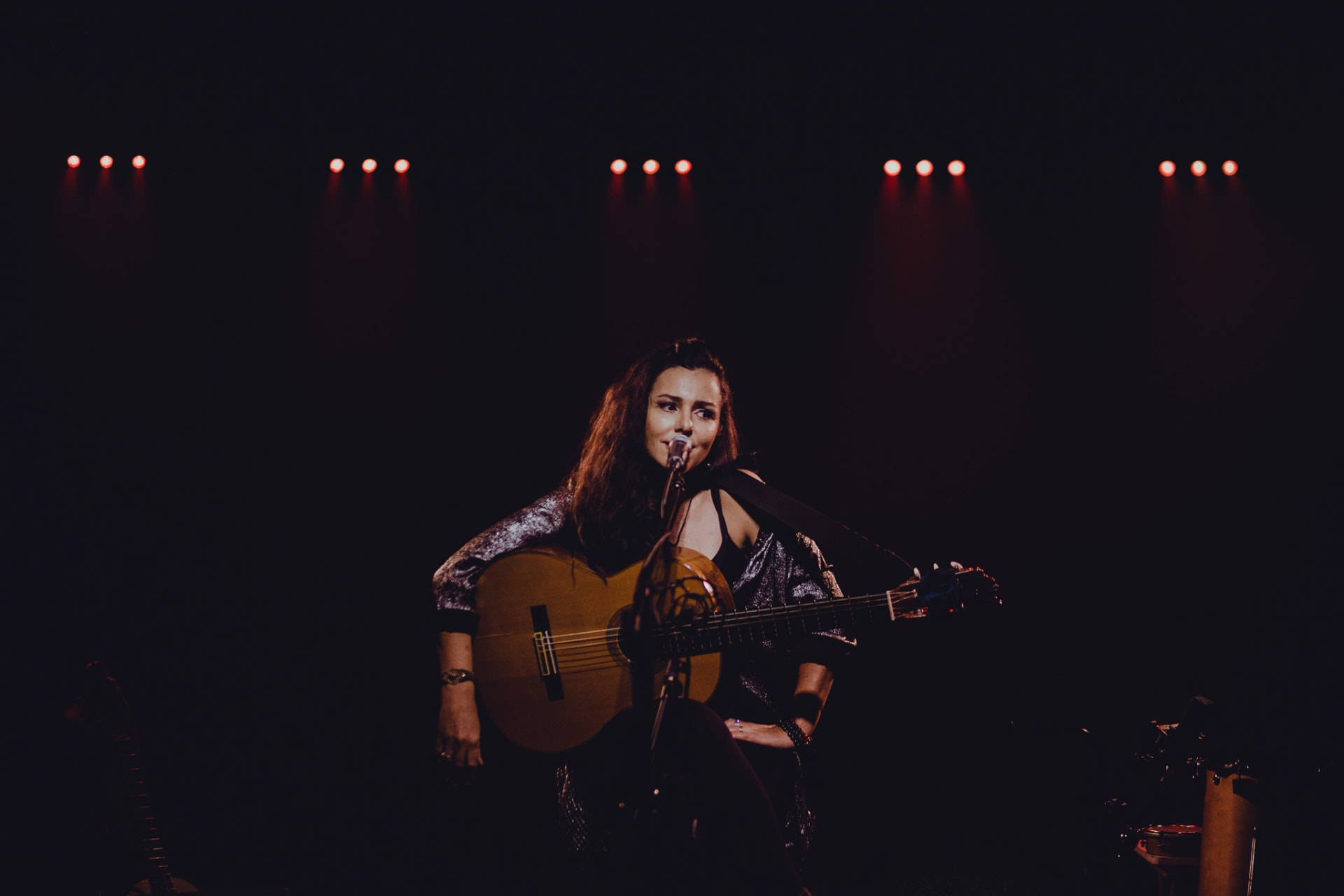 Carolina Zingler ao microfone com violão sob luzes vermelhas