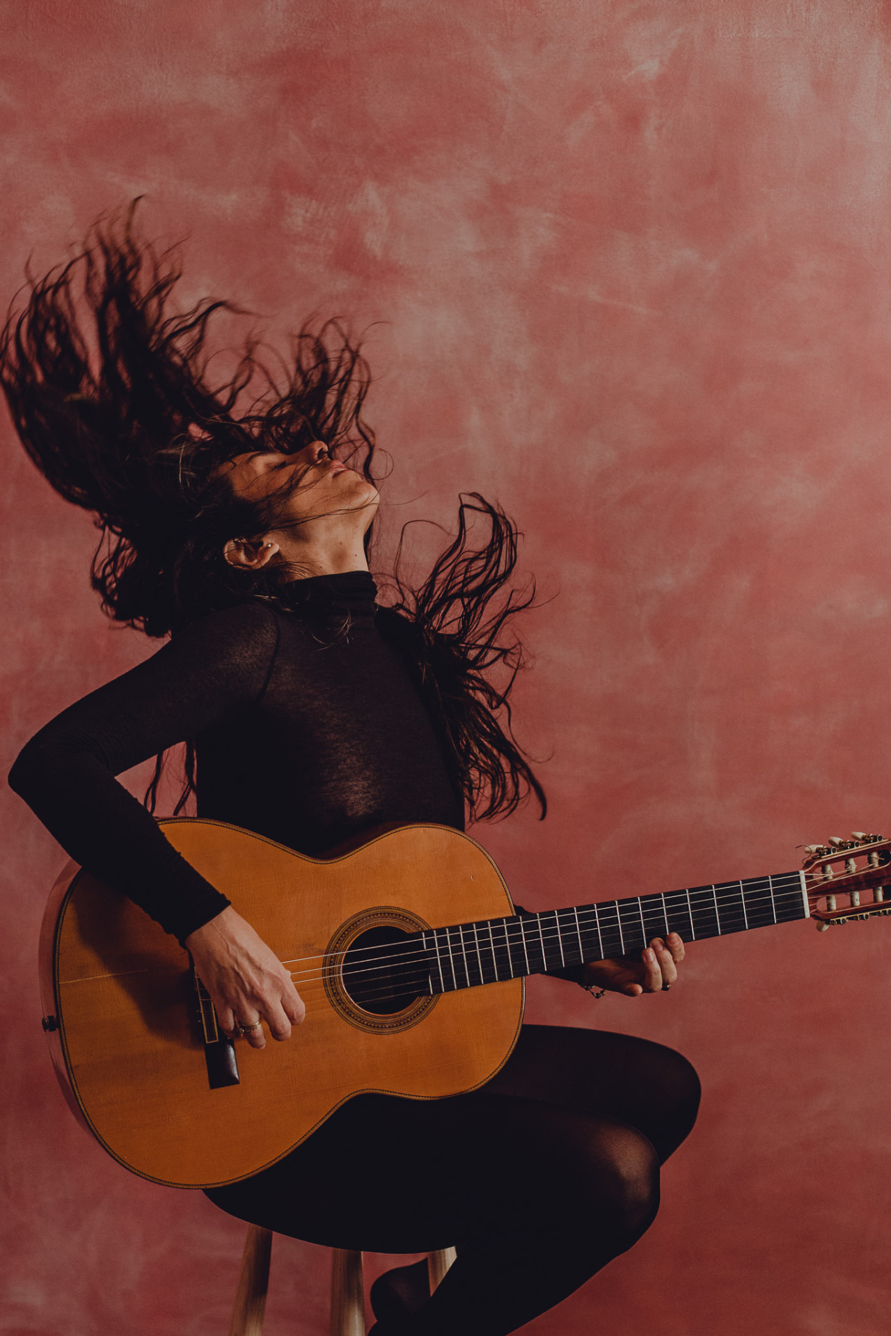 Carolina Zingler em pose dinâmica, cabelo ao vento, sobre sofá vermelho