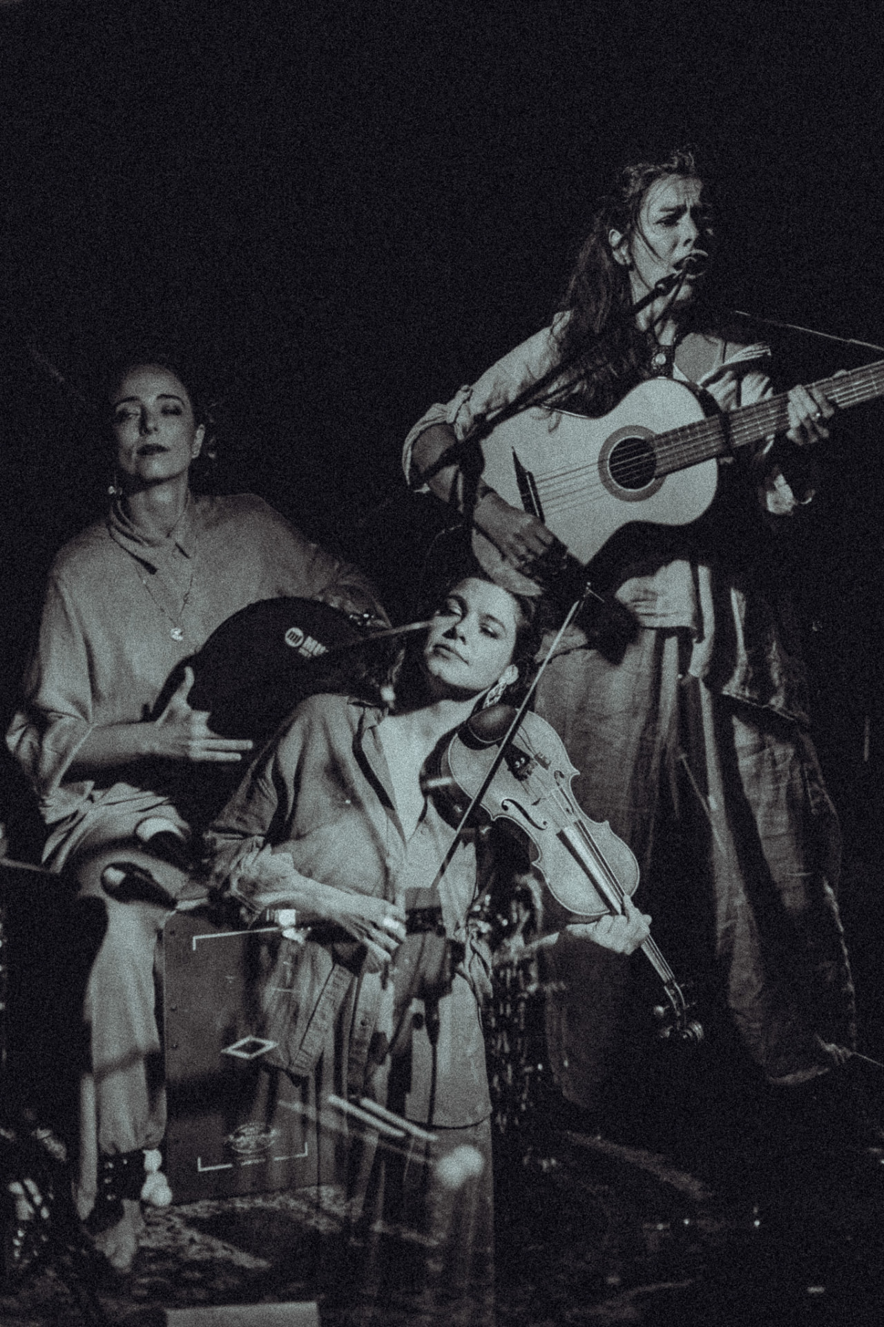 Trio em palco a preto e branco: violão, percussão e violino